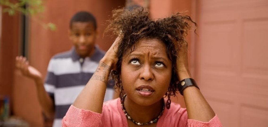 frazzled mom grabbing hair in annoyance as teen boy shrugs in background