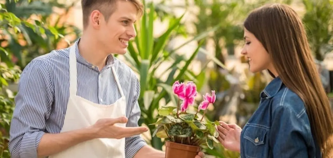 teenage boy working a job at a garden store showing an orchid to a teenage girl