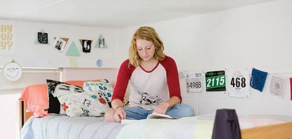 college student sitting on the top bunk of a dorm room surrounded by posters