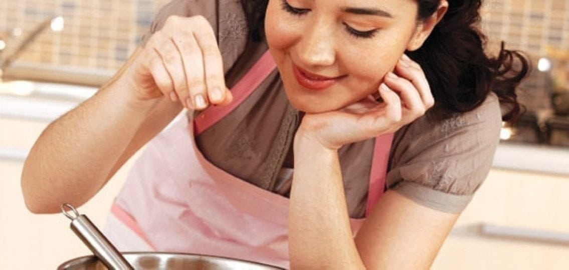 teen girl wearing a pink apron putting some salt into a pot