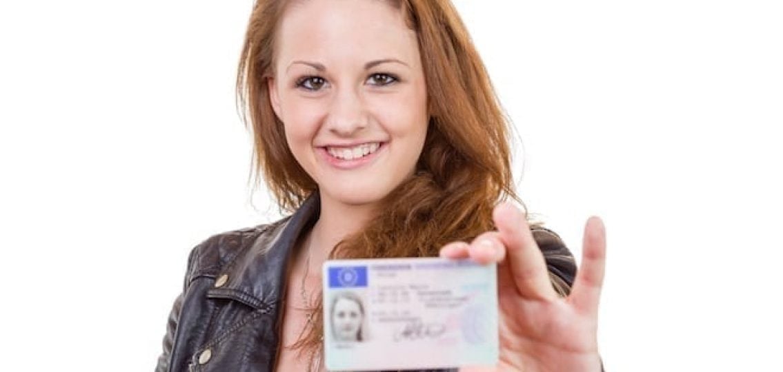 teenage girl holding up her drivers license and smiling white background