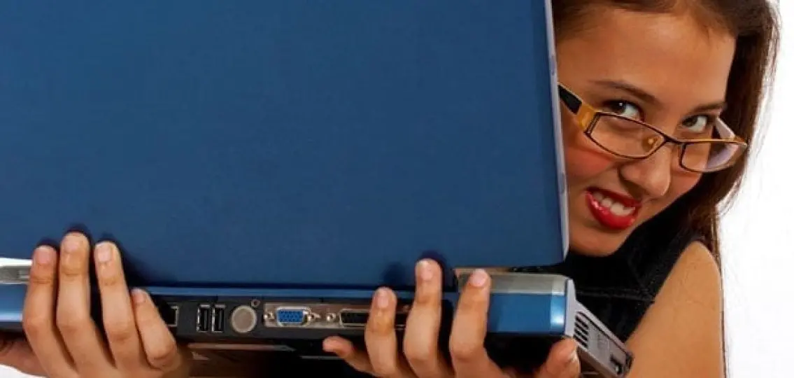 smiling girl peaking head from behind a blue laptop
