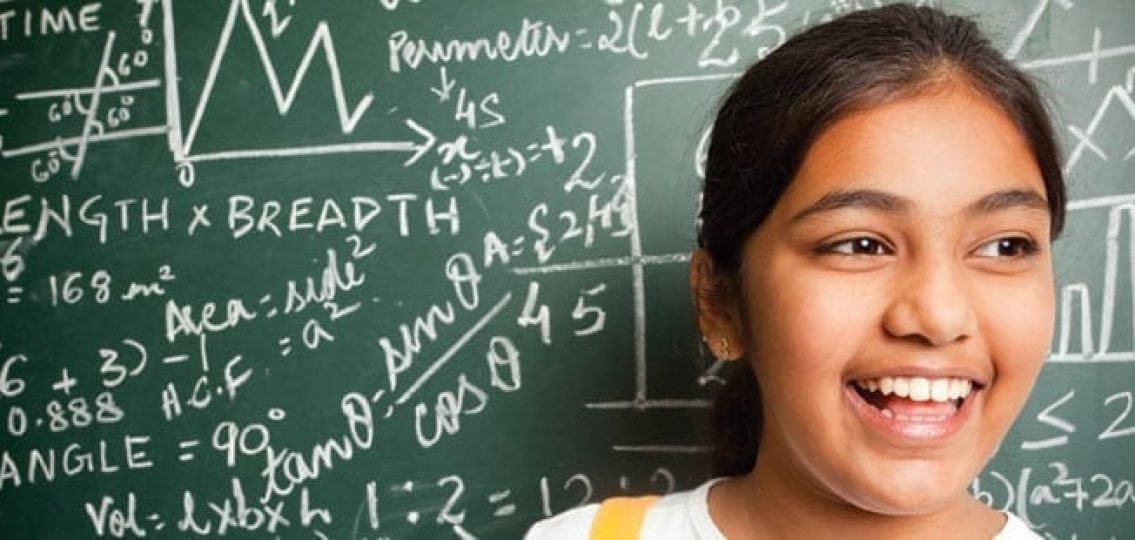 smiling middle school girl in front of a full chalkboard full of math problems