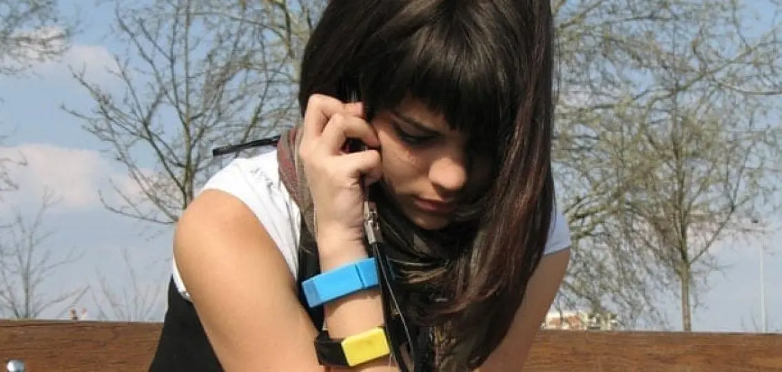 depressed teenage girl sitting on a bench outside on the phone