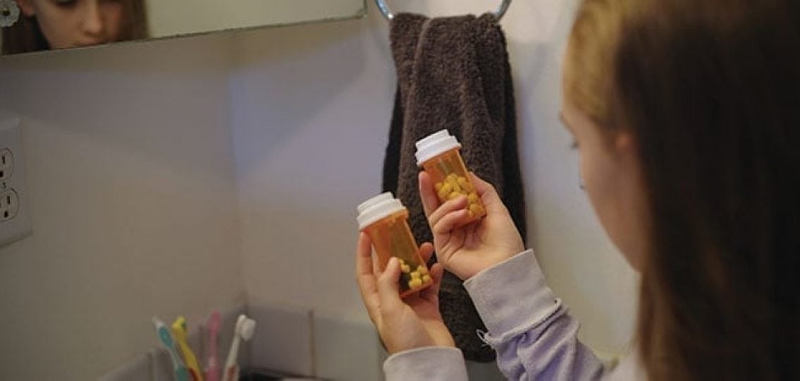 teen girl in a bathroom holding up two prescription pills