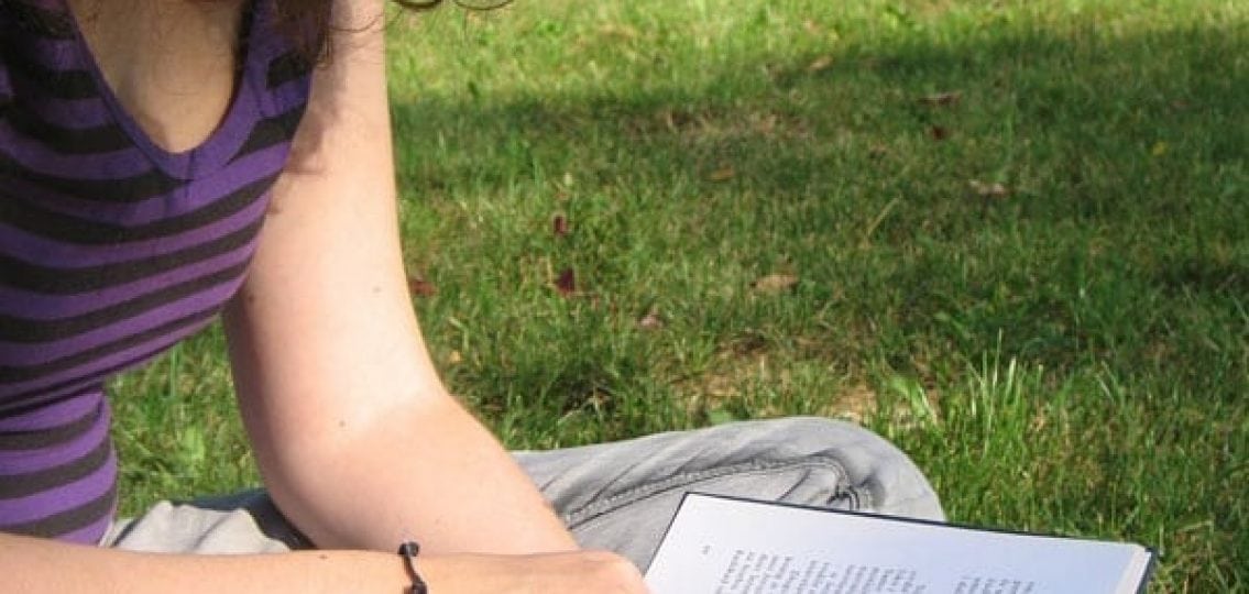 girl reading a book outside in the grass
