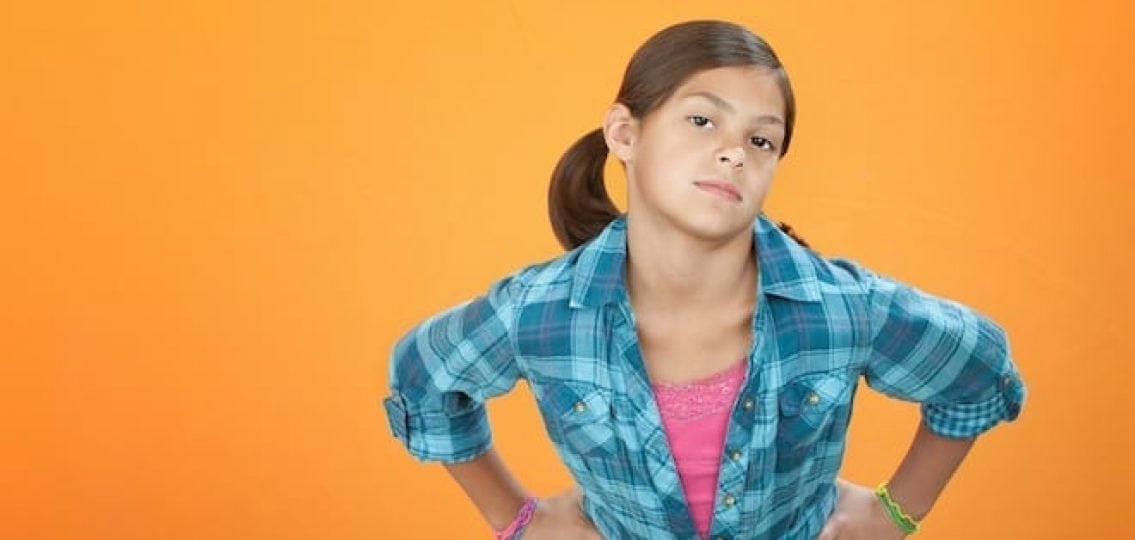 teen girl with attitude with her hands on her hips orange background