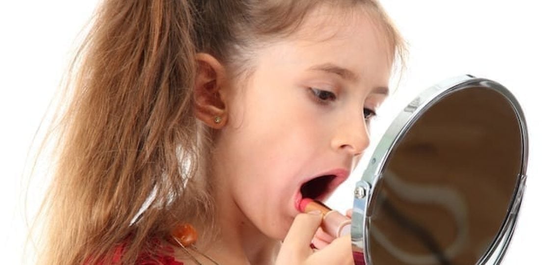 young girl putting on lipstick in the mirror
