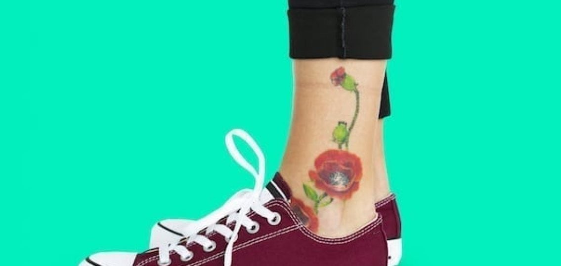 close up of a teen girls ankle tattoo teal background