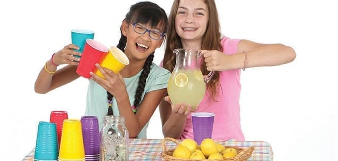 teen girls running a lemonade stand with solo cups and a jug of lemonade