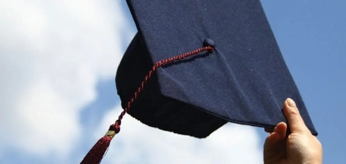 a graduation cap being held in the air outdoors