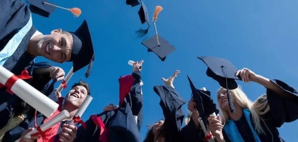 teenage graduates throwing their caps and showing off their diplomas