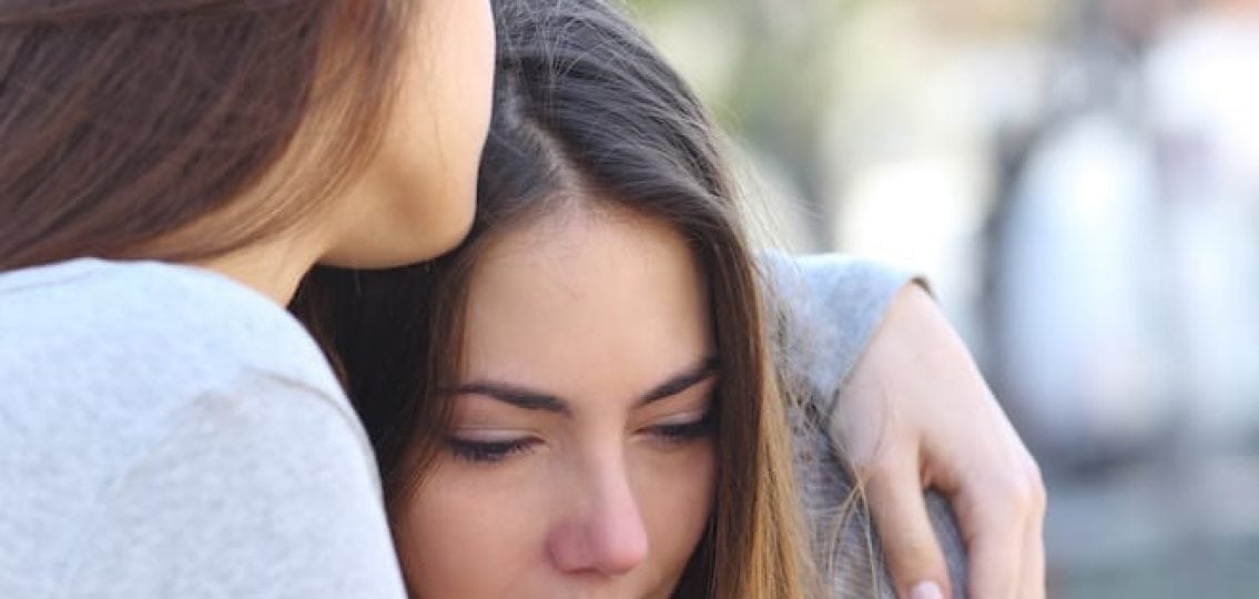 grieving teenage girl being held by a friend or parent
