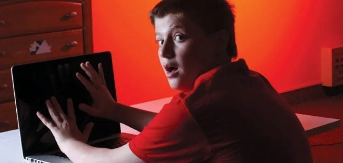 surprised teenage boy trying to hide his computer screen from the camera