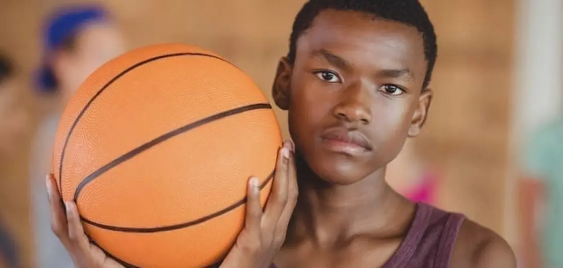 serious teenage boy with basketball looking into camera, background blurred