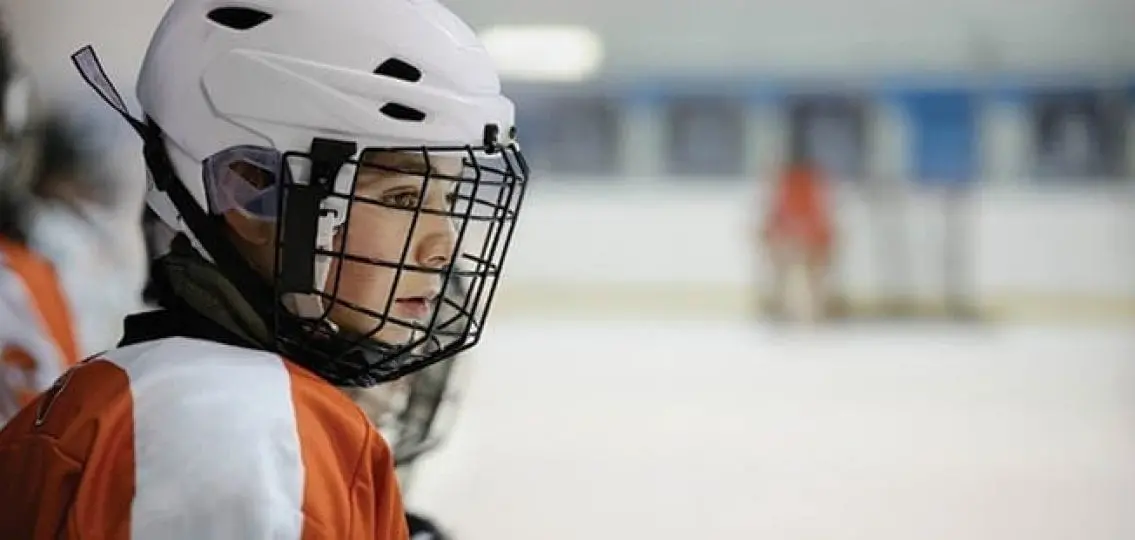 sad teen boy in hockey gear sitting on the sideline of hockey rink