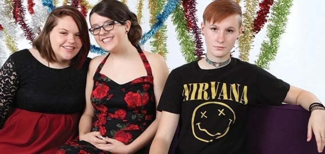 siblings taking holiday pictures two in dresses one in punk rock clothes