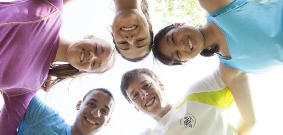 teenagers in a huddle dressed for sports smiling down at the camera