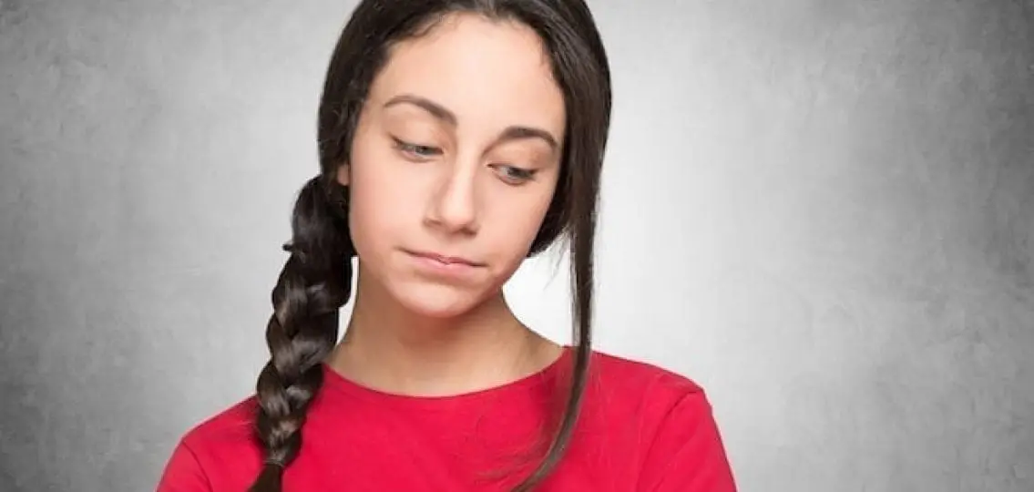 insecure teen looking shyly away from camera gray background