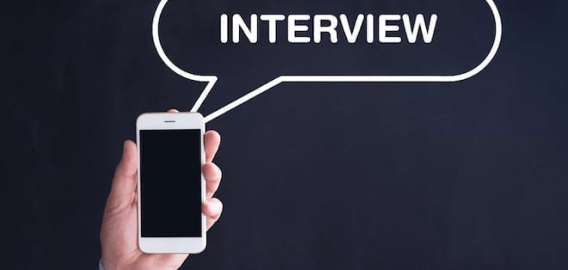 hand in a suit sleeve holding a phone with a speech bubble that says interview