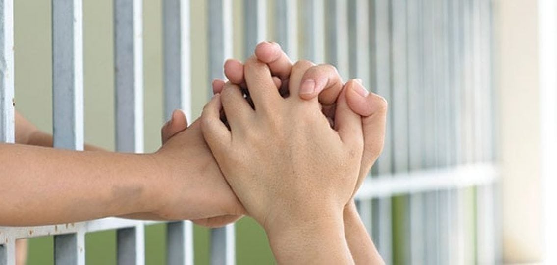 hands reaching through jail bars and holding hands