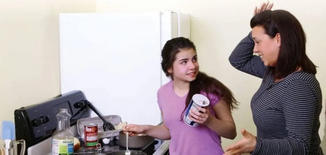 distressed teen girl cooking a meal while her mom looks upset
