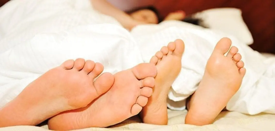 couple in bed under covers focus on their feet at the bottom of the bed