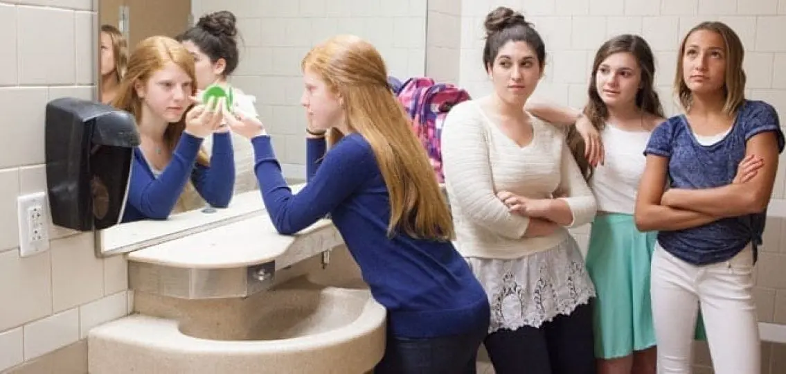 middle school girls in the bathroom three girls glaring at other girl putting on makeup