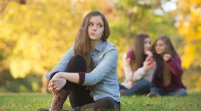 scowling teen girl while girls point at her in the background