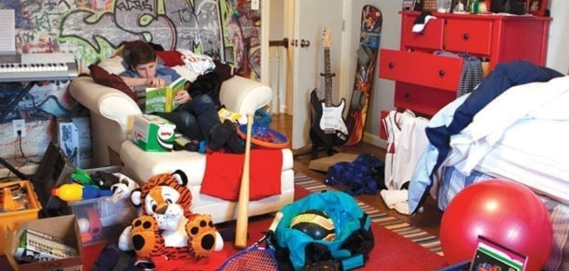 teenage boy in his messy room puled with clothes and toys and boxes