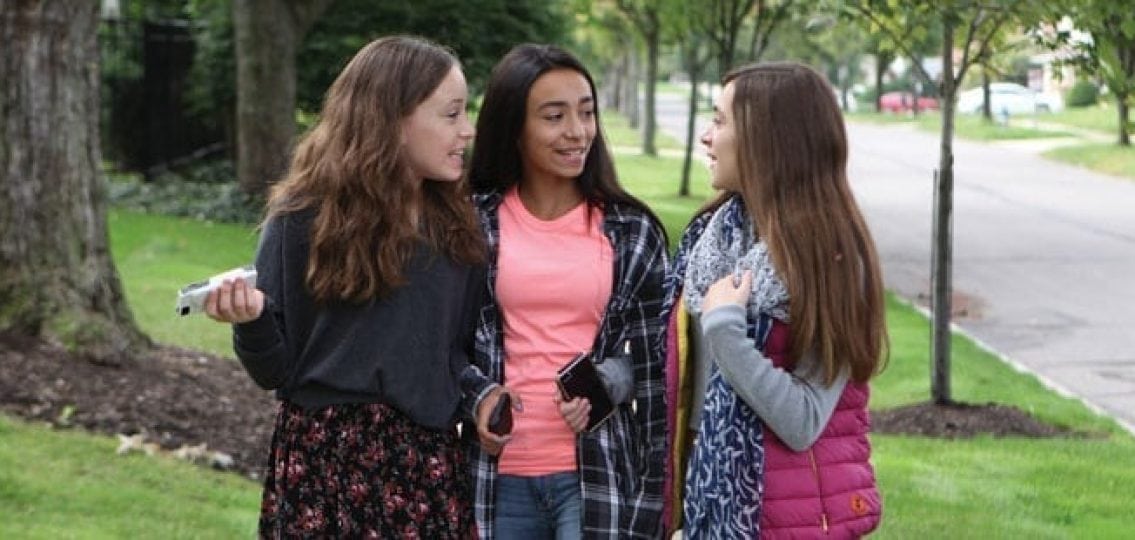three middle school girls walking down the sidewalk and gossiping