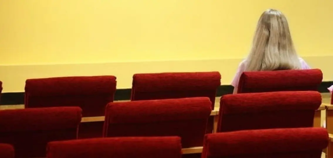 single mom sitting alone in an auditorium facing away