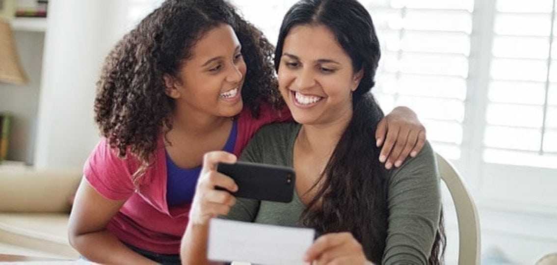 mom and daughter smiling taking a picture of a check with an online banking app
