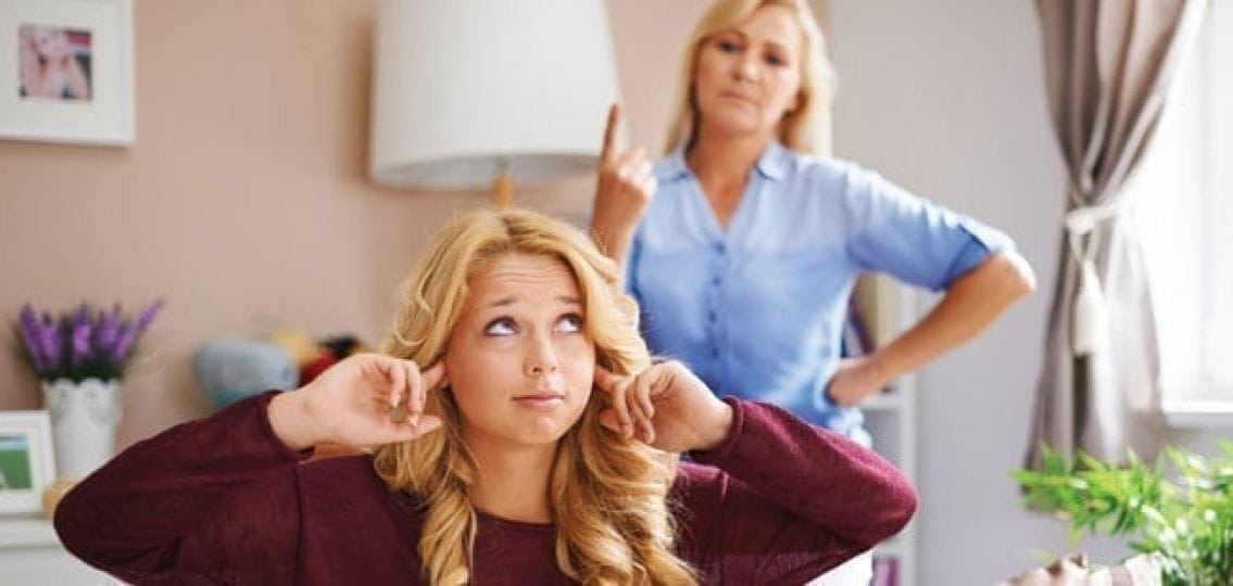 teen girl rolling eyes and covering ears while mom gets mad in the background
