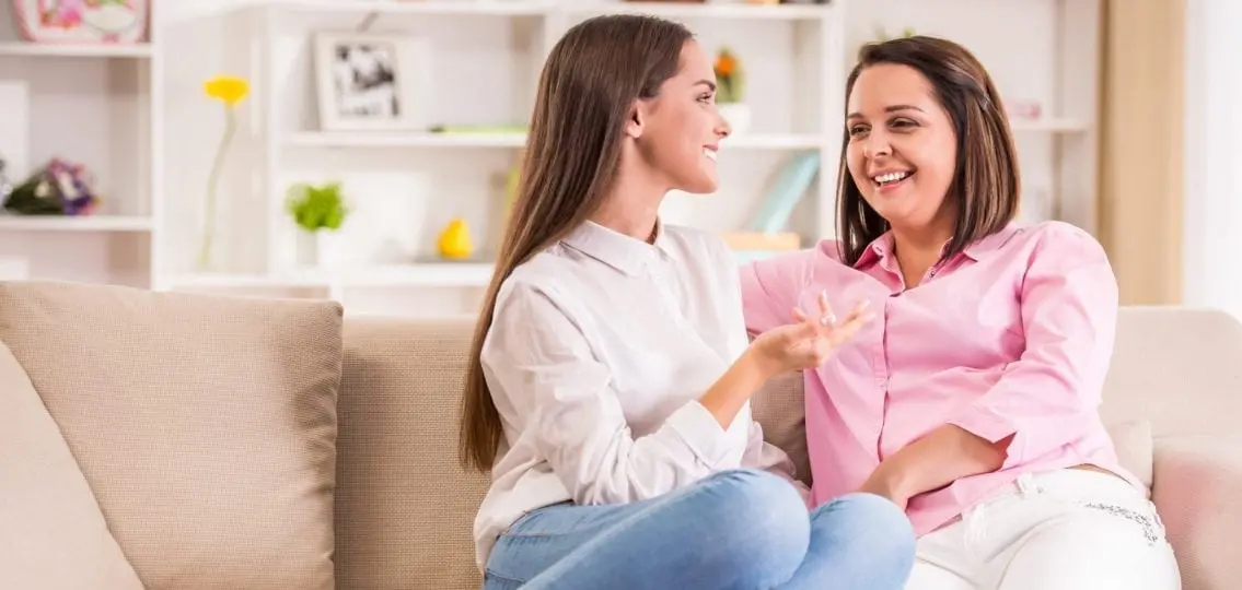 smiling mother and teen daughter sitting together on the couch and talking
