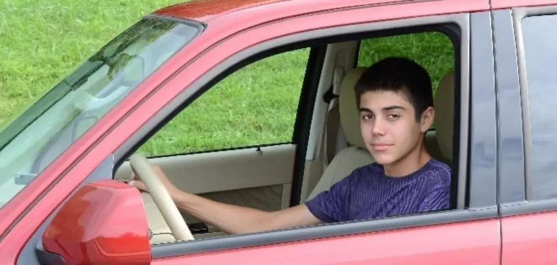 a young teenager behind the wheel in a red car