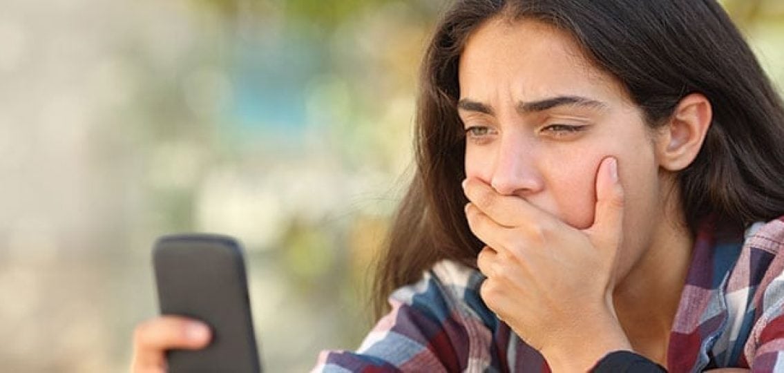 upset girl on her phone looking at a text and covering her mouth