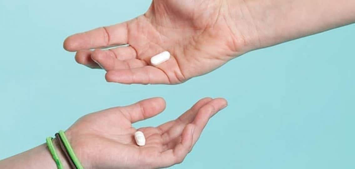 close up of hands holding pills on a blue background