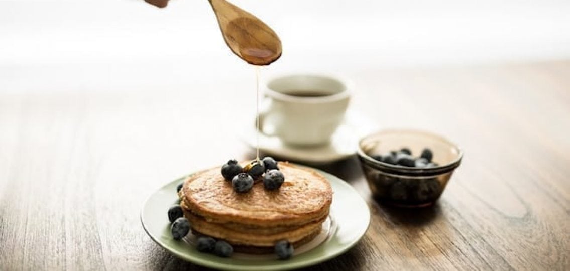 pancakes on a plate with blueberries being topped with maple syrup