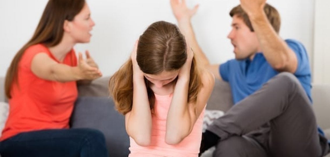 two parents fighting on a couch as a teen girl covers her ears