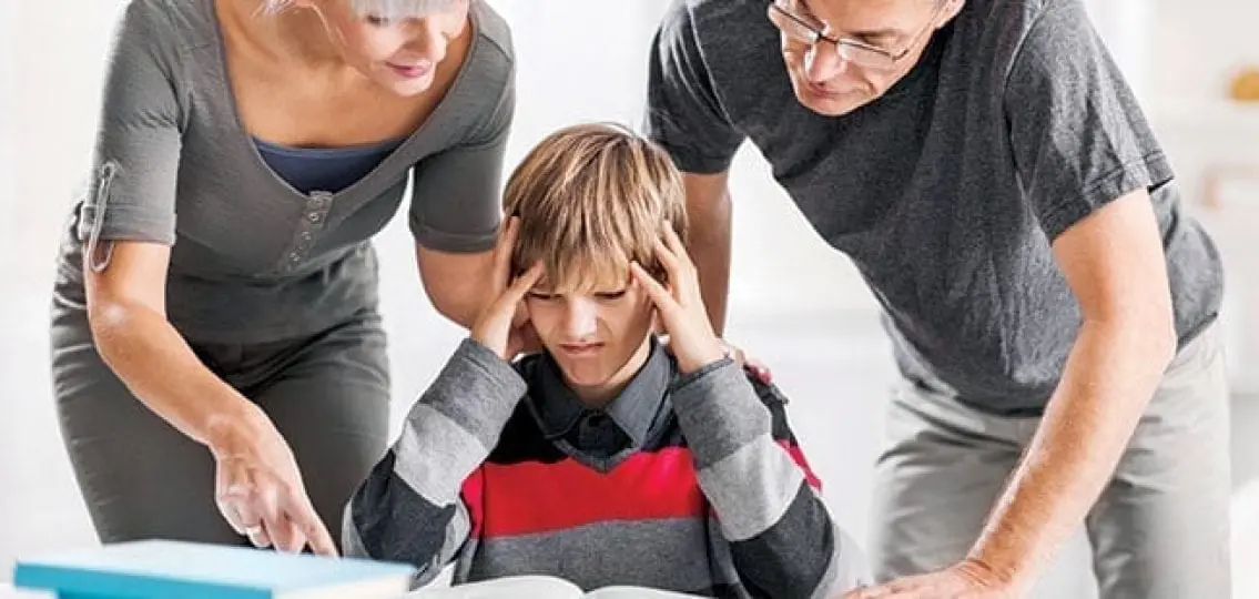 frustrated middle school boy glaring at homework as his mom and dad attempt to explain