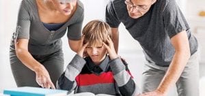 frustrated middle school boy glaring at homework as his mom and dad attempt to explain