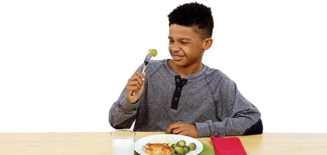 picky teenage boy upset at brussel sprouts on his plate of chicken and rice