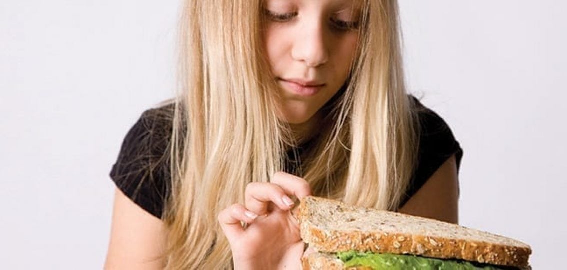 unhappy teenage girl picking at a sandwich