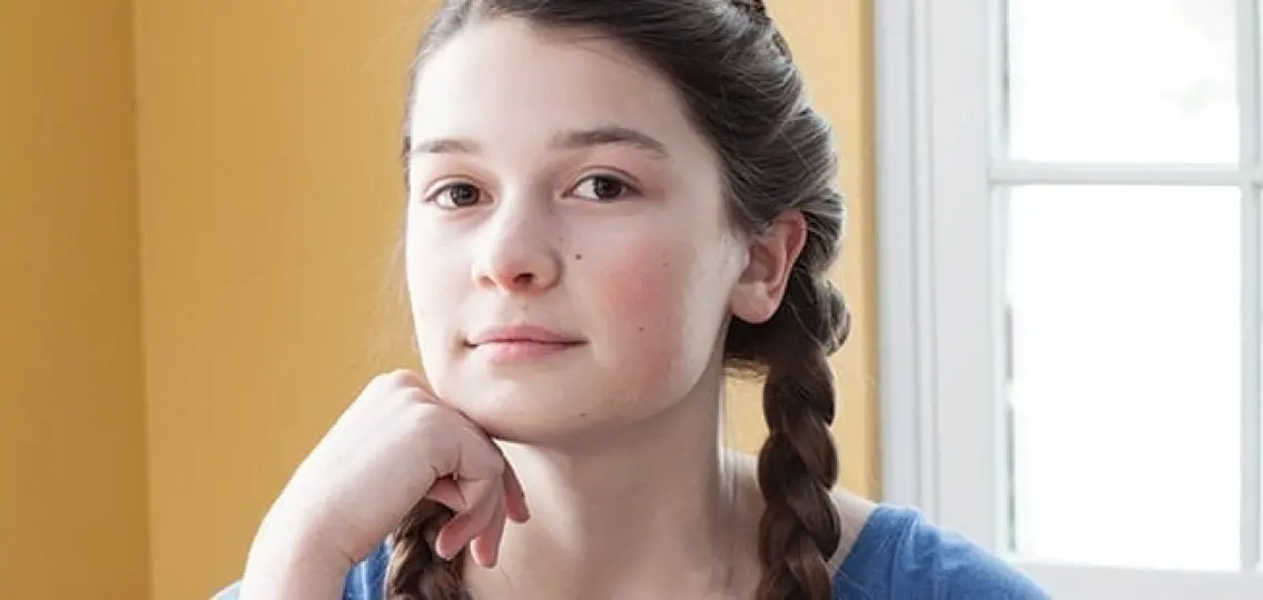 teenage girl with a small smile looking at the camera indoors