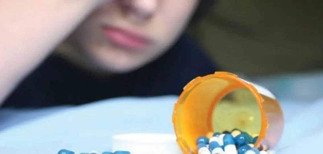 prescription drugs spilled on a bed with a teen blurred in the background