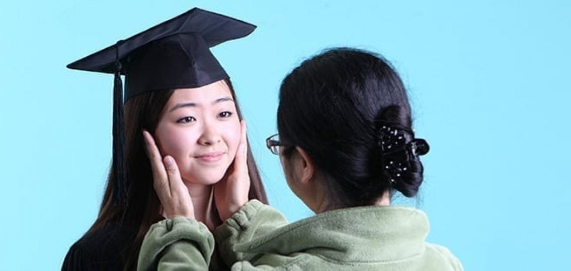 mom holding her daughter's face with graduation cap blue background