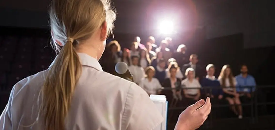 teen public speaking standing at a podium in front of an audience