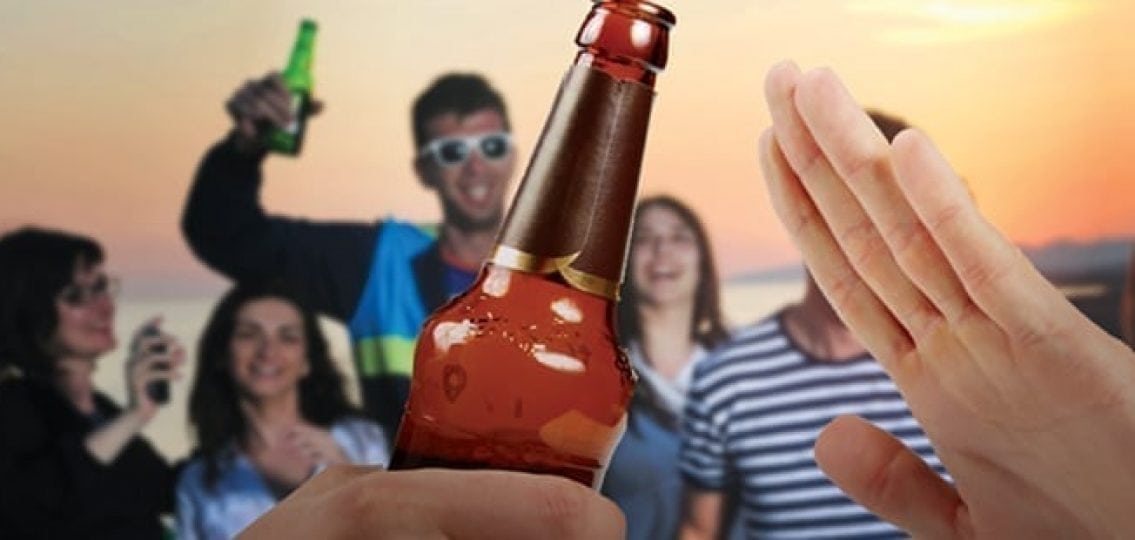 hand refusing a beer as teens drink and party on a beach in the background