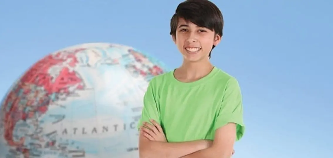 smiling teen boy in front of a globe on a blue background